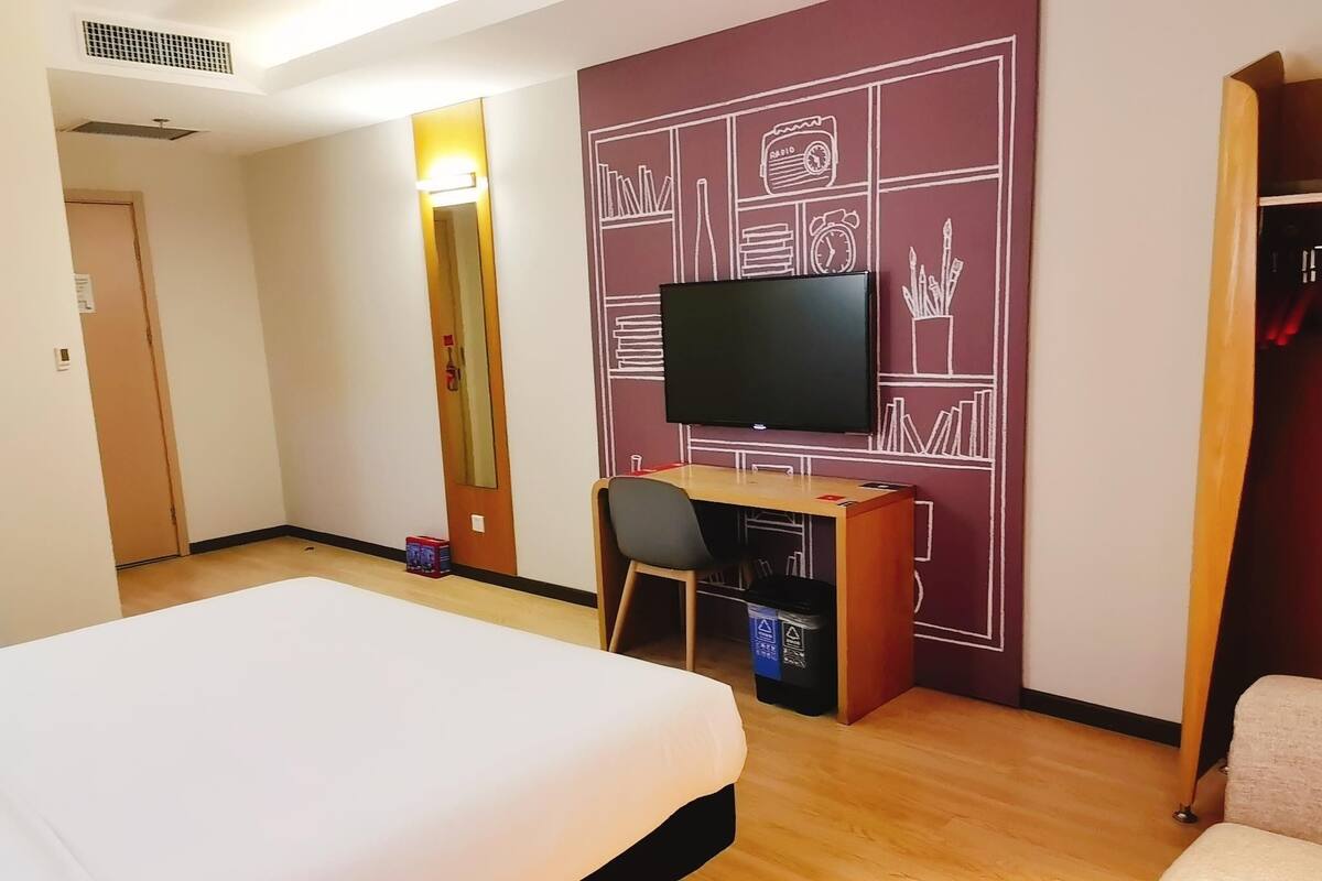 A hotel room with a bed, a desk with a chair, a television, and a wall with a geometric design.