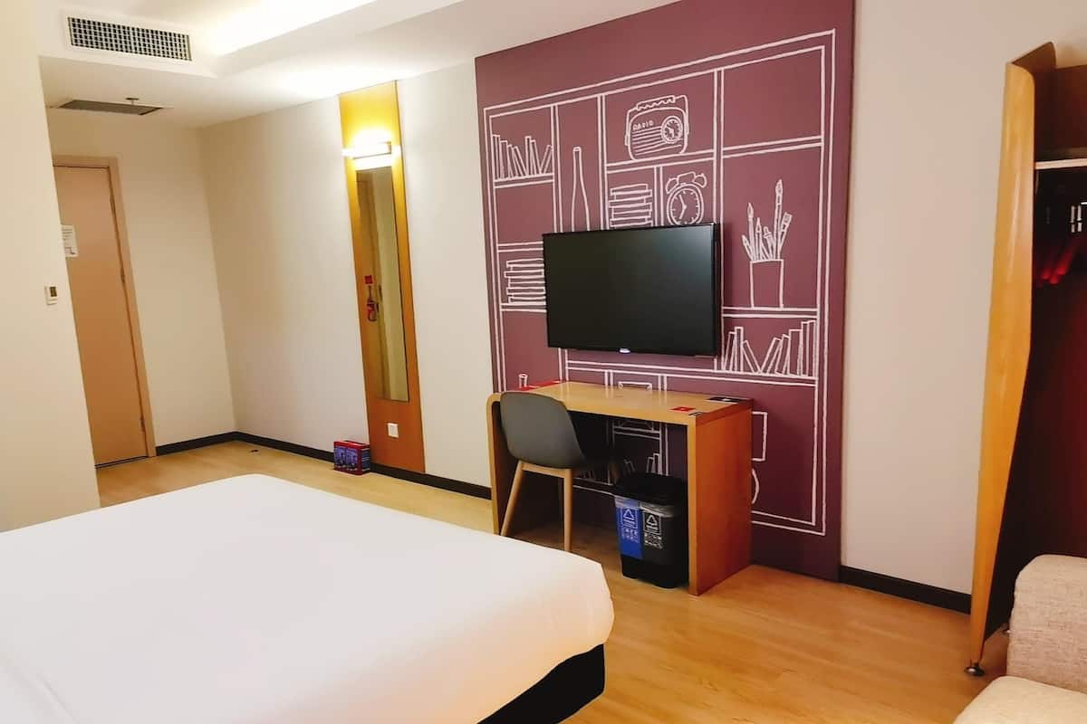 Hotelkamer met een bed, een bureau met stoel, een televisie en een muur met een geometrisch ontwerp.