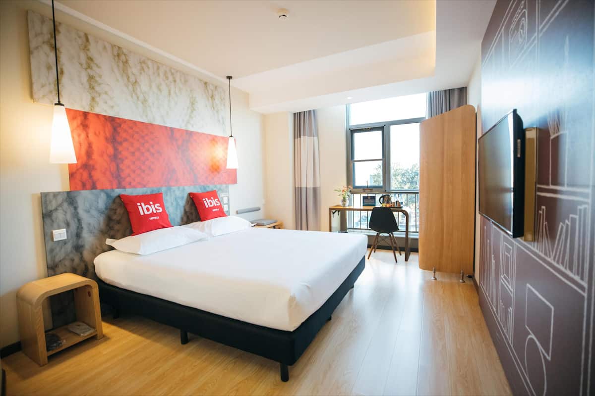 Een hotelkamer met een groot bed, een bureau, een televisie en uitzicht op het landschap.
