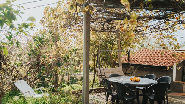 A patio with a table and chairs, surrounded by greenery and a pergola. - Remarkable 4-bed Apartment in Joppolo (Joppolo)
