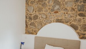 A bedroom with a stone wall, a bed with a patterned bedspread, a nightstand with a lamp, and a ceiling light. - Remarkable 4-bed Apartment in Joppolo (Joppolo)