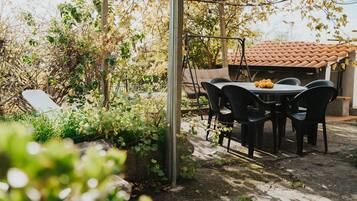Patio esterno con tavolo e sedie, immerso nel verde e dotato di una pergola.