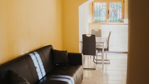 A living room with a sofa, a dining table with chairs, and a window with a view of the outdoors. - Remarkable 4-bed Apartment in Joppolo (Joppolo)