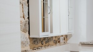 A bathroom with a white sink, a white cabinet above it, and a stone wall. - Remarkable 4-bed Apartment in Joppolo (Joppolo)