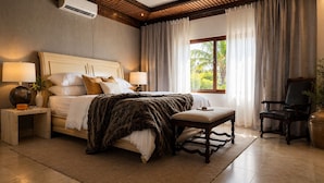 Un dormitorio con cama, mesitas de noche, una silla, una ventana con cortinas y un equipo de aire acondicionado.