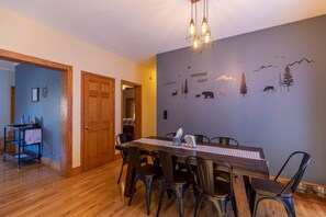 A dining area with a wooden table and chairs, a wall mural with wildlife, and a kitchen in the background.