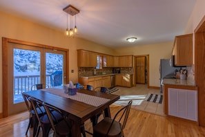 A spacious kitchen with wooden cabinets, a dining area with a large table and chairs, and a view of a snowy deck through large sliding glass doors.