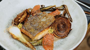 A plate of food with a fish, vegetables, and a garnish on a marble table.