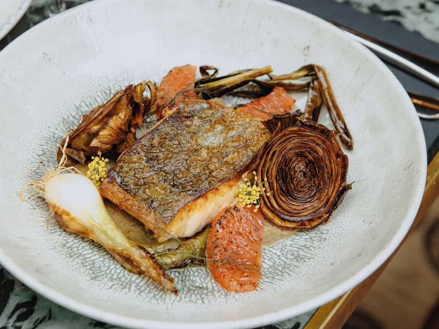 A plate of food with a fish, vegetables, and a garnish on a marble table.