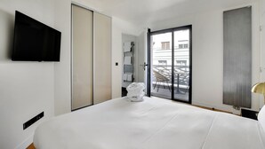 A hotel room with a bed, a TV mounted on the wall, a sliding door, and a view of the outside balcony.