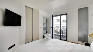 Habitación de hotel con una cama, televisor montado en la pared, puerta corrediza y vistas al balcón exterior.