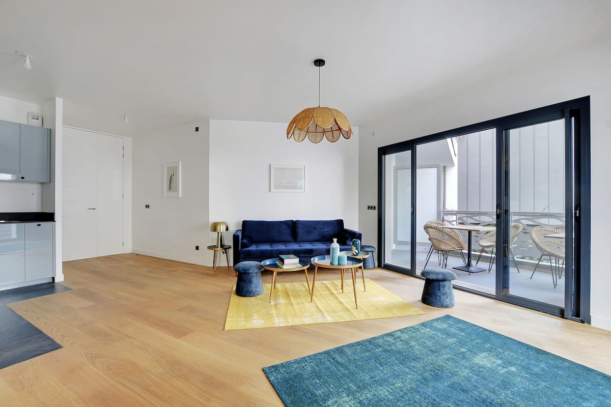 Una sala moderna con un sofá azul, mesas redondas de centro y un ventanal grande.