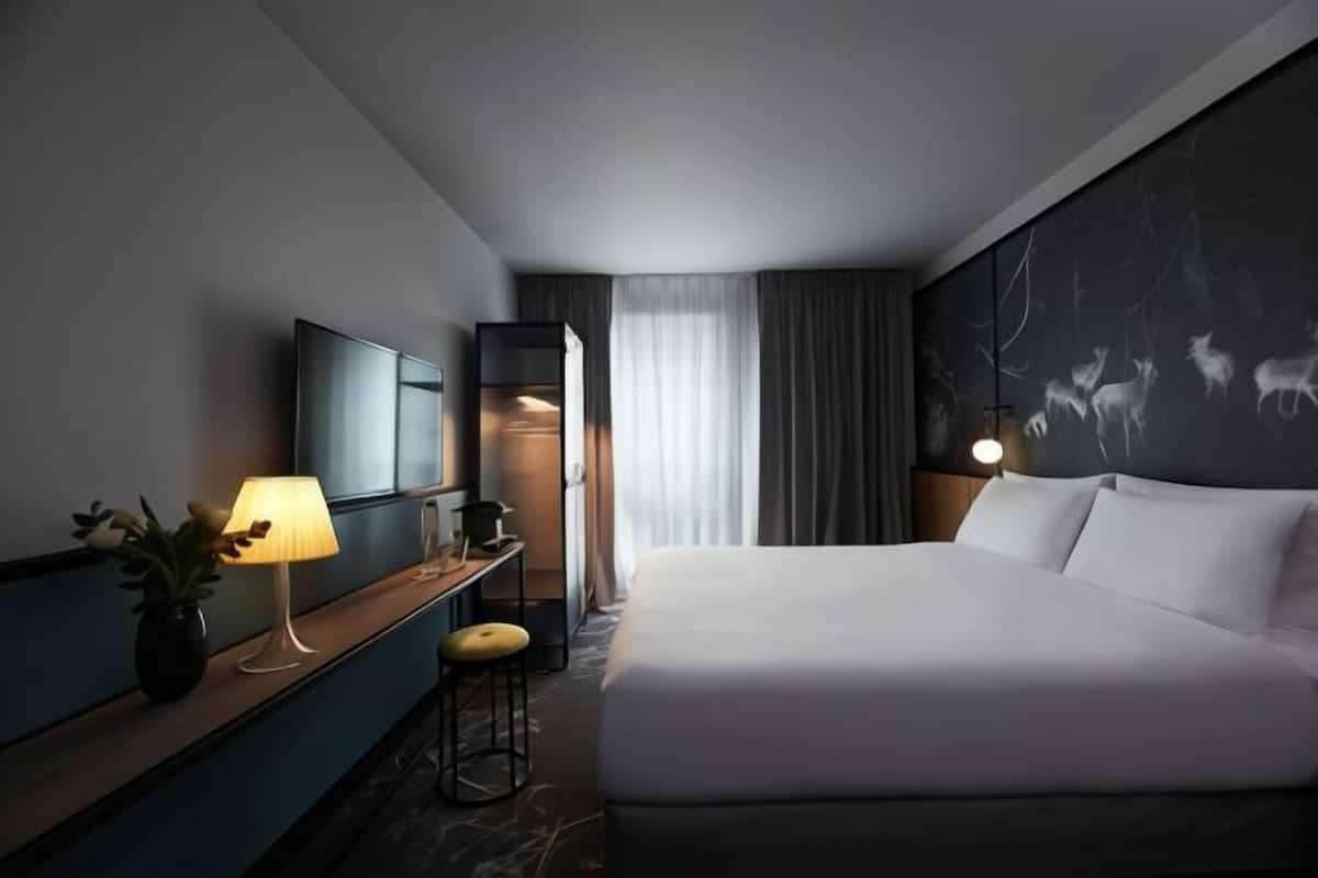 Habitación de hotel con cama, escritorio con lámpara, televisor y un mural temático de naturaleza en la pared.