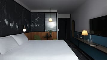 Une chambre d’hôtel moderne avec un grand lit, un bureau avec une lampe, une petite table avec une plante et un grand miroir.