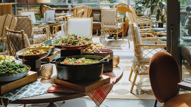 A dining area with wicker furniture, a variety of dishes, and a view of greenery outside. - Drawing House (Paris)