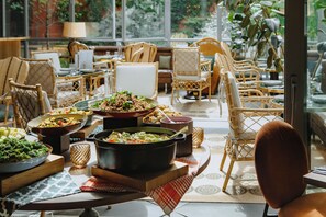 A dining area with wicker furniture, a variety of dishes, and a view of greenery outside. - Drawing House (Paris)
