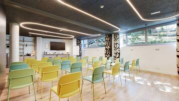 Una sala conferenze con file di sedie, un grande schermo e vista sul verde all'esterno.