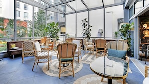 A spacious indoor area with wicker furniture, glass walls, and a view of the city. - Drawing House (Paris)