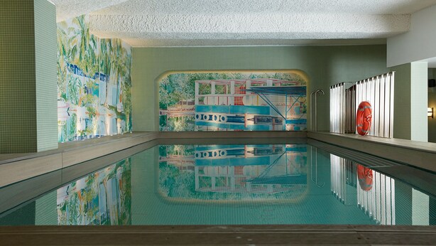 An indoor swimming pool with a mural of a tropical scene and a lifebuoy on the wall.