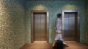 A modern elevator with a textured wall and a person walking towards it.