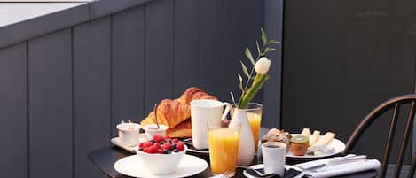 A dining table with breakfast items on a balcony overlooking a cityscape.