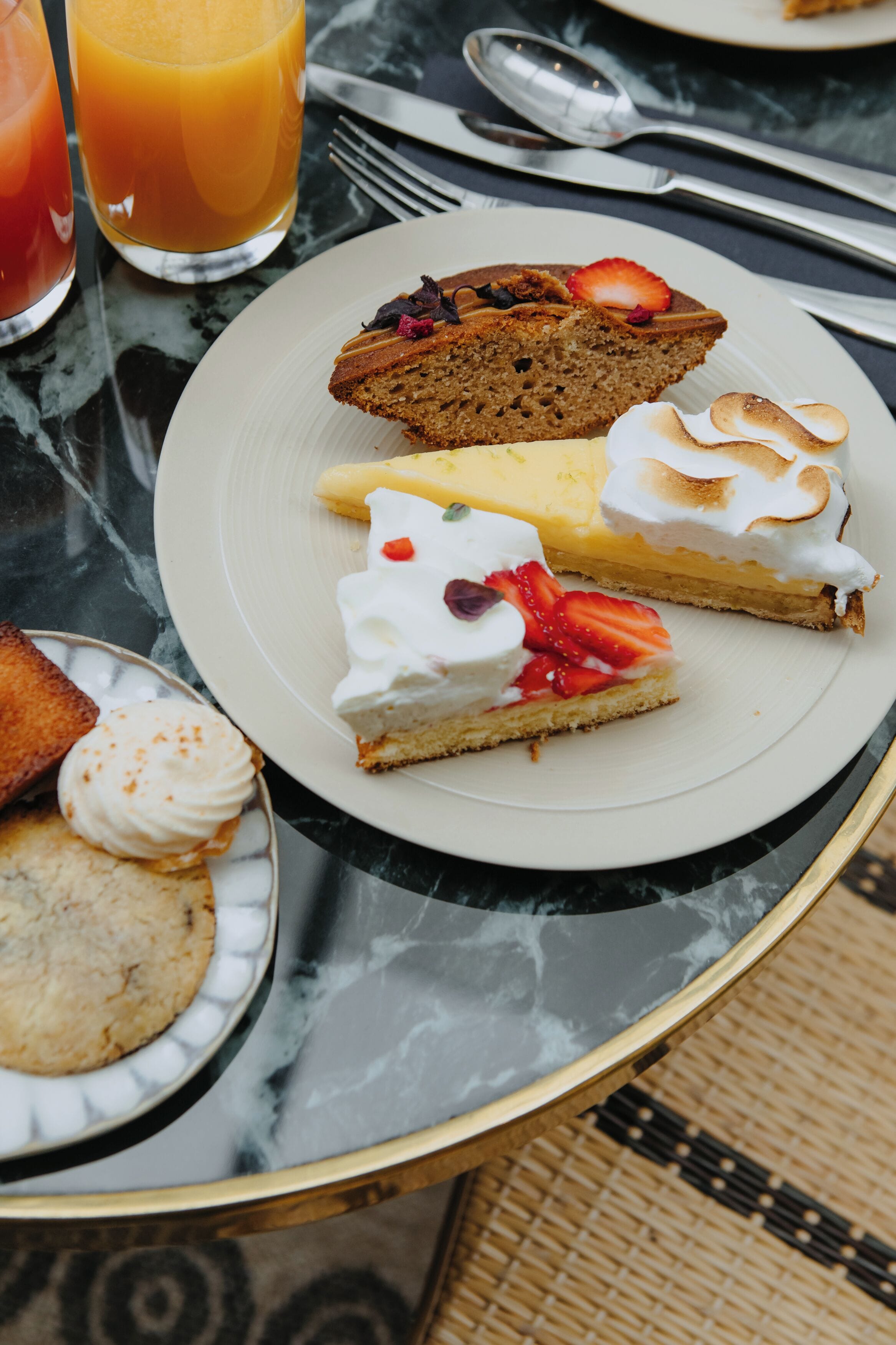 Une table en marbre dressée pour le petit-déjeuner, avec une assiette de viennoiseries, un verre de jus d’orange, une fourchette et une cuillère.