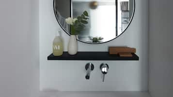 Un bagno con uno specchio rotondo, uno scaffale nero con articoli da toilette, un asciugamano e un lavandino.