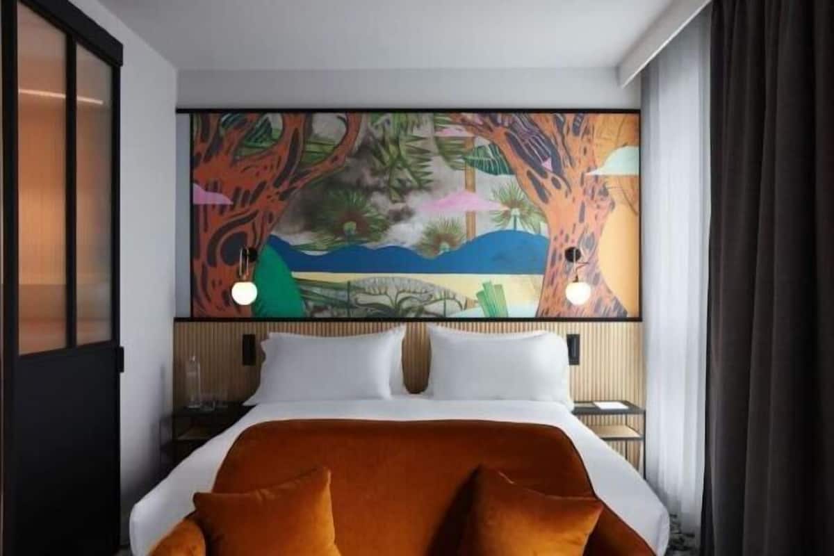 Habitación de hotel con una cama, un cuadro grande en la pared y una mesita de noche con una lámpara.