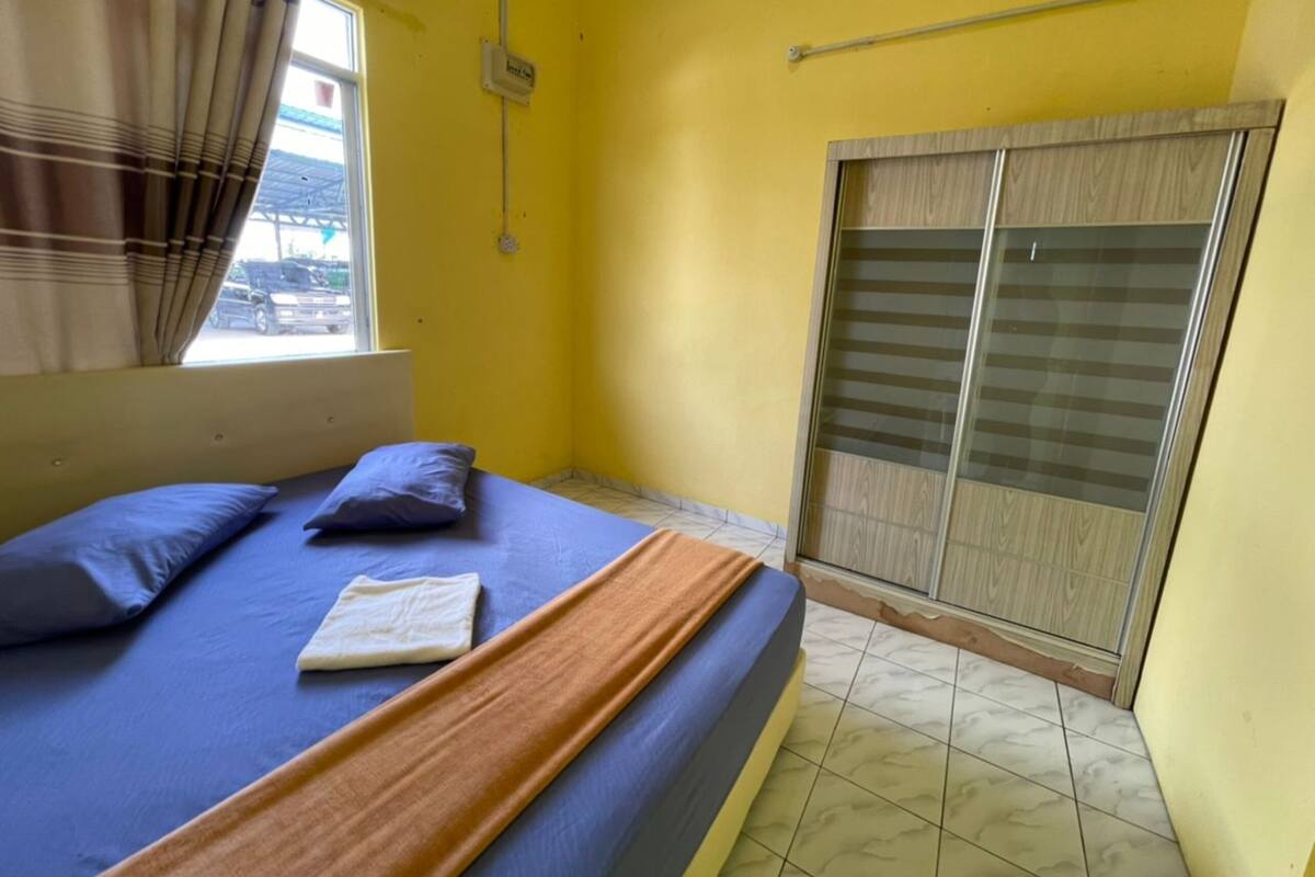 A bedroom with a bed, pillows, a blanket, a window with curtains, a wall socket, and a sliding door.
