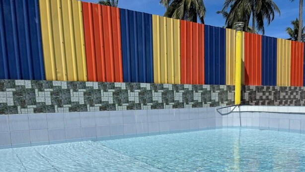 Piscina com deck revestido e parede colorida com listras verticais em azul, amarelo, vermelho e laranja.