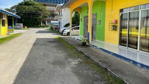 Um edifício com fachada amarela e verde, uma área de estacionamento com carros e uma grua de construção ao fundo.