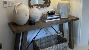 Een houten console tafel met een spiegel, twee witte vazen, een lamp en een mand.