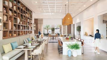 A spacious hotel lobby with a central dining area, a large bookshelf, and a modern ceiling design.