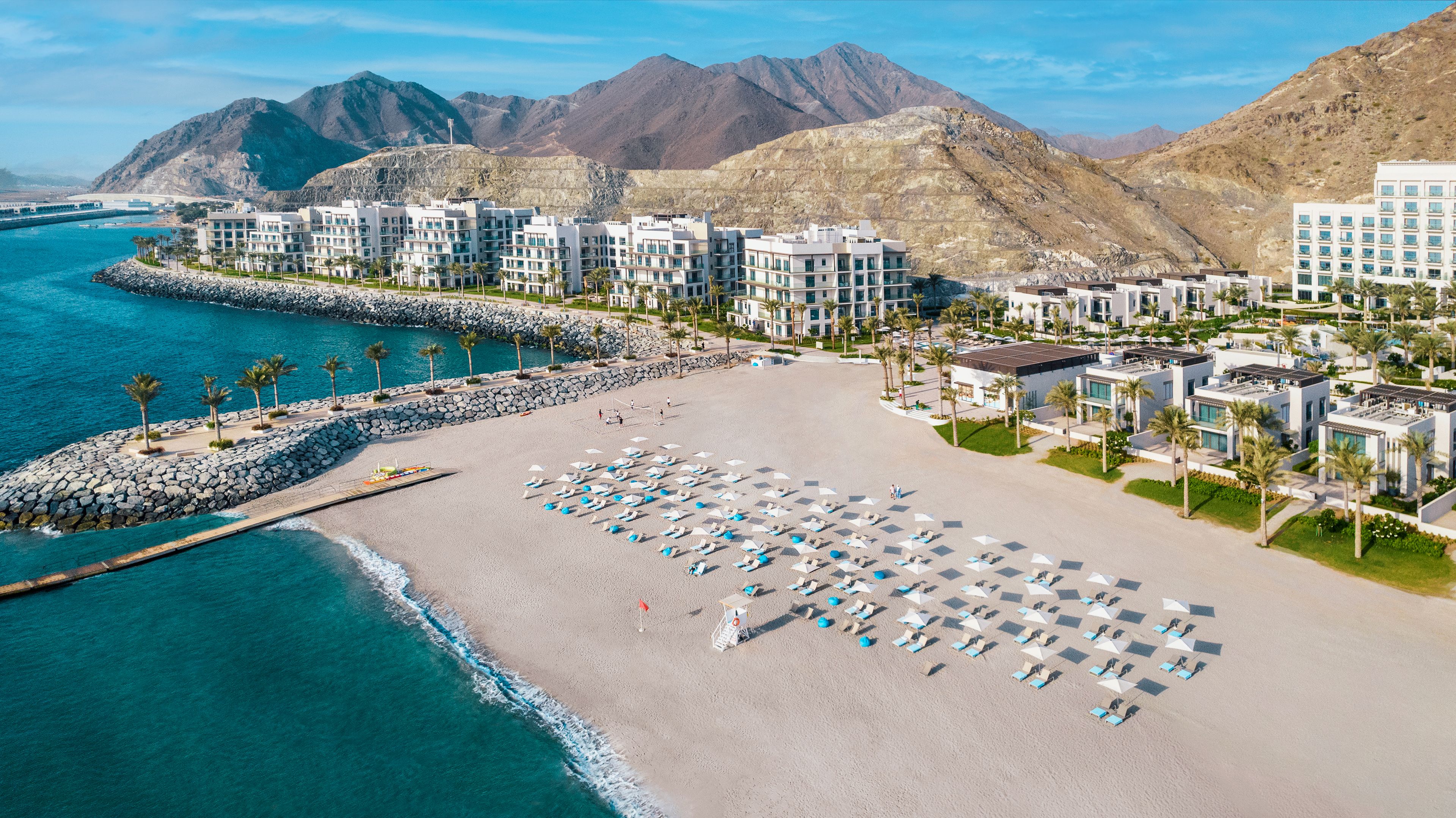 A coastal hotel with multiple buildings, a sandy beach, and a rocky shoreline.