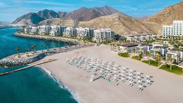 A coastal hotel with multiple buildings, a sandy beach, and a rocky shoreline.