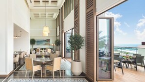 A spacious dining area with a large table and chairs, a potted plant, and a view of the ocean through large sliding doors. - Address Beach Resort Fujairah (Al Aqah)