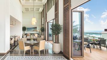 A spacious dining area with a large table and chairs, a potted plant, and a view of the ocean through large sliding doors.