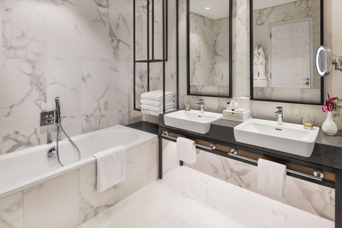 A modern bathroom with a large bathtub, two sinks, and a mirror with a built-in light.