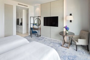 A hotel room with two beds, a desk with a chair, a round table with a chair, a TV mounted on the wall, and a small vase with flowers.