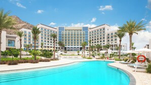 A hotel with a swimming pool, palm trees, and a mountainous backdrop. - Address Beach Resort Fujairah (Al Aqah)