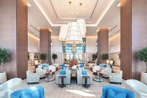 A spacious lobby with modern seating, a central chandelier, and a view into the kitchen area. - Address Beach Resort Fujairah (Al Aqah)