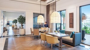 A modern hotel lobby with a dining area, large windows, and a view of the outdoors. - Address Beach Resort Fujairah (Al Aqah)
