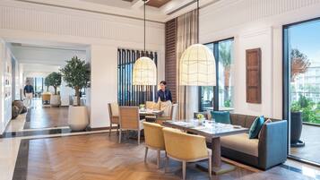 A modern hotel lobby with a dining area, large windows, and a view of the outdoors.