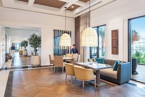 Un hall d’hôtel moderne doté d’un espace repas, de grandes fenêtres et offrant une vue sur l’extérieur.