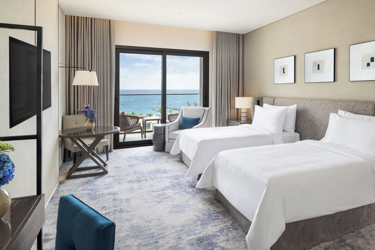 Une chambre d’hôtel avec deux lits, un bureau, une chaise et une vue sur l’océan.