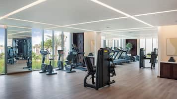 A modern gym with various exercise equipment, large windows, and a wooden floor.