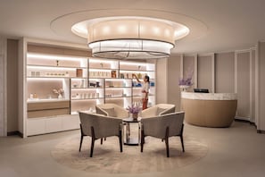 A modern reception area with a central chandelier, a reception desk, and a seating area with chairs and a table. - Address Beach Resort Fujairah (Al Aqah)