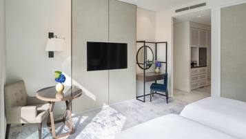 A modern hotel room with a bed, a desk with a chair, a TV, a mirror, and a small table with a vase.