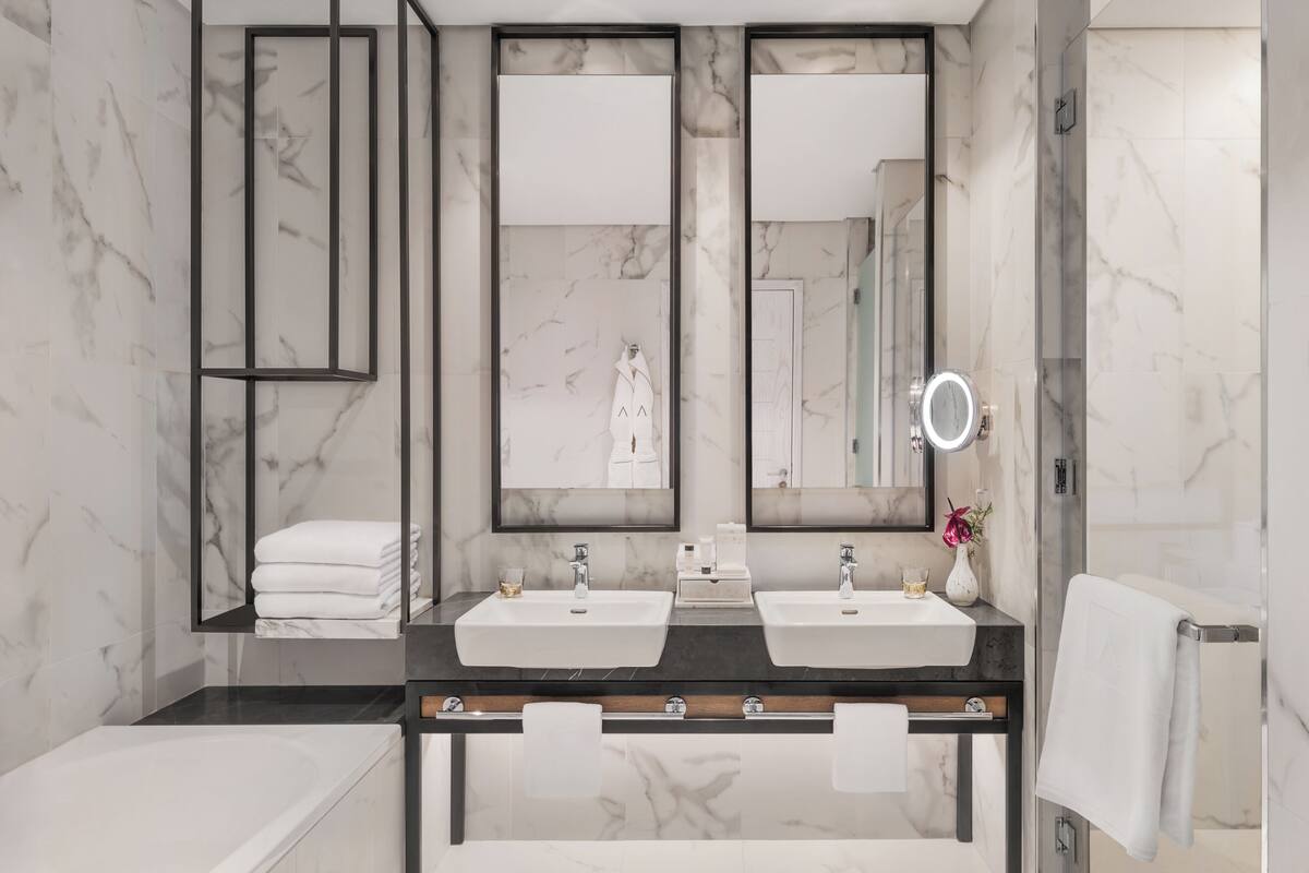 A modern bathroom with two sinks, a large mirror, and a bathtub.