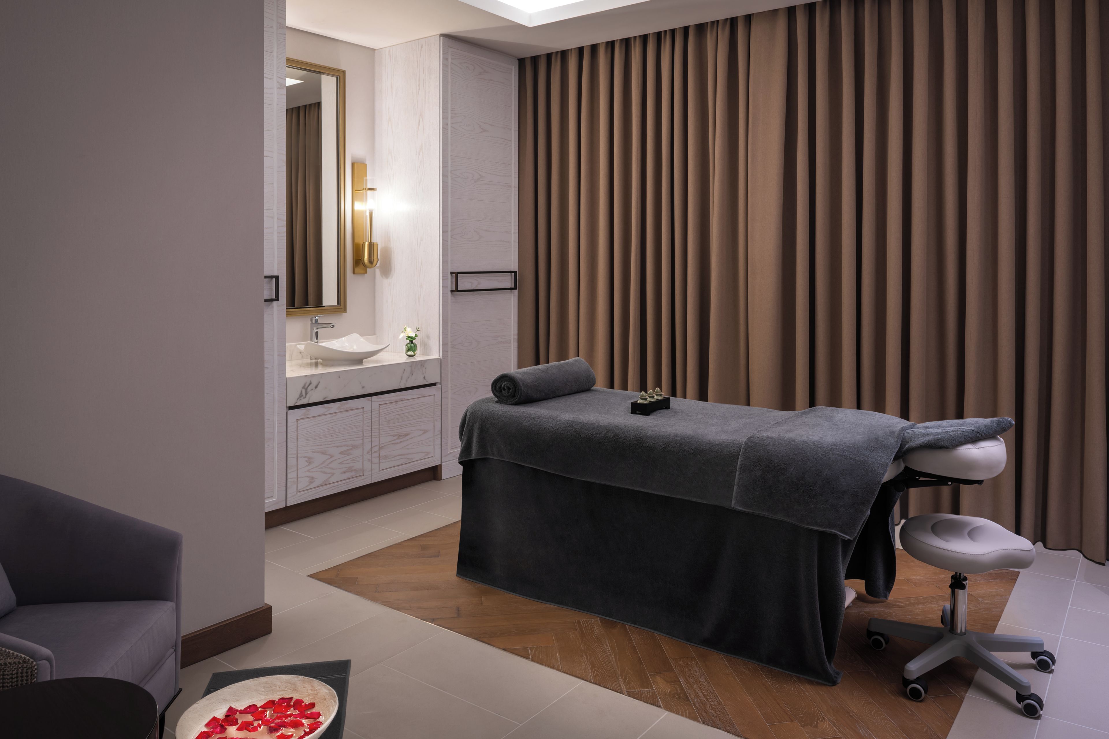 Une salle de spa moderne équipée d’une table de massage, d’un fauteuil, d’un lavabo et d’un miroir.